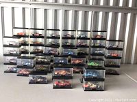 Photo shows large assortment of Hot Wheels NASCAR die-cast cars in display cases arranged on a table against a wall.
