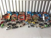 Photo showing a collection of multiple model motorcycles including Harley-Davidson, Muscle Machines, Adventure Wheels, some in packaging others displayed outside.