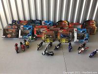 Photo showing multiple model motorcycles including boxed and unboxed, with riders in various colors. Some are sealed in their original Maisto and Joyride packaging.