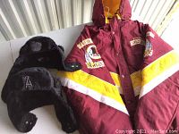 Photo of maroon Washington Redskins NFL Starter jacket with logos on sleeves and chest and yellow interior lining, and two black sherpa NHL style trapper hats, one with 'A' logo patch