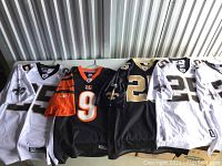 Five NFL jerseys laid out on a surface, primarily New Orleans Saints jerseys and one Cincinnati Bengals jersey, size large.