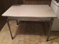 Full view of the table showing the Arborite laminate top and metal legs on a tiled floor in a room corner.