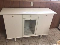 Front and side view of a white wood cabinet with two side doors and a center glass door, showing overall condition and design.
