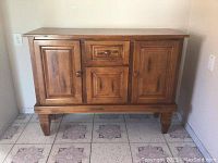 Wooden cabinet front view showing two doors and central drawer and door.