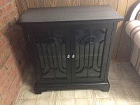 Closed black wooden cabinet with decorative glass panel doors and silver knobs.