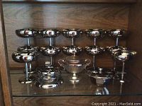 Front view of 10 silver goblets arranged on two shelves, plus additional silver bowls and containers below
