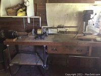 Wide shot of wooden workbench including two bench grinders mounted and drill press.