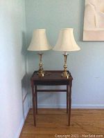 Full view of wooden table with two brass lamps.
