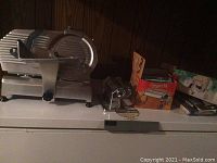 Electric meat slicer and pasta maker items displayed on freezer top