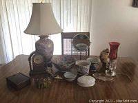 Photo showing all items grouped on a table including lamp, clock, ceramic bowls and pots, red glass lamp, and decorative boxes.