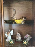 Wide view of upper shelf showing glass swan, yellow bowl with dragonfly, and two green glass dishes