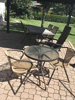 Outdoor patio set showing large rectangular metal table with chairs and small round glass table with woven armchairs.
