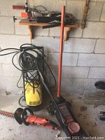 Wide view of the lot showing yellow pressure washer, black hydraulic floor jack with red handle, and orange handheld tool on concrete floor against cinder block wall.