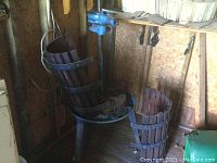 Wine press and two wooden baskets with visible wear and rust in a wooden shed corner.