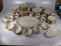 Full set of Lenox Rose Manor china laid out, showing the variety of plates, cups, saucers, bowls, and serving pieces in white china with pink rose floral design and gold trim.