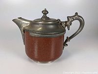 Side view of the antique Manning Bowman enamelware tea kettle showing reddish-brown speckled enamel and metal handle and lid.