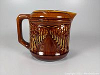View of the brown glazed ceramic pitcher showing the tree lined path relief and handle