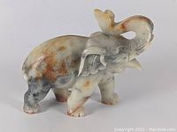 Front and side angled view of the carved elephant statue showing the natural coloration and detailed features.