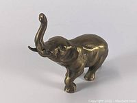 Angled side view of cast brass elephant figurine with raised trunk on plain background.
