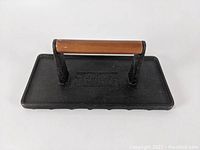 Top view of the panini press weight showing the black cast iron surface and attached wooden handle