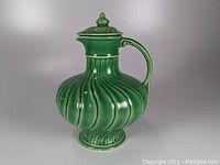 Front view of the green pottery covered jug showing handle and lid with glossy swirled ribbed body design.