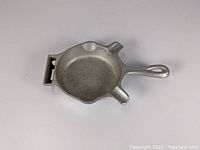 Aluminum Griswold ashtray shown from top angle, displaying skillet shape, matchbook holder, and cigarette rests.