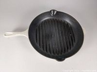 Top view showing black ridged cooking surface with pour spouts and white enameled handle.