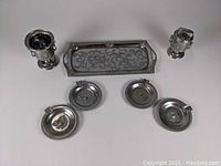 Top-down photo of all seven pieces in the chrome metal smoking set showing lighter, smoker's cup, four ashtrays, and tray.