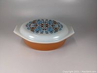Side view of Pyrex casserole dish with orange base and decorated white lid with Navajo pattern
