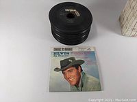 Top view of a stack of 45 RPM vinyl records showing Imperial record label on one and Elvis Presley double record with picture sleeve in front.