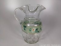 Clear blown glass lemonade pitcher with floral enamel band, wavy rim, and applied handle