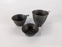 Three vintage tin measuring cups arranged with handles facing outward, showing size and shape.
