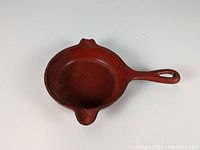 Top angled view of red enamel cast iron ashtray showing interior and handle with hanging hole.