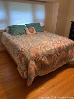 View of the queen size bed fully made with colorful patterned linens and several pillows including teal decorative ones