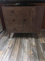 Full front view of the wood cabinet showing the three drawers on the left and the door on the right. Cabinet is on metal legs.