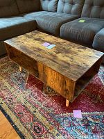 Top and side view of rustic wooden coffee table on patterned carpet in living room, showing the wood grain texture and storage compartment.