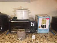 Photo showing a white Crock Pot slow cooker, Krupps toaster oven with control panel, ceramic candle warmer, and boxed 2-in-1 drink dispenser on countertop.