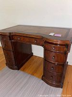 Full view of wooden desk with leather top and seven drawers, showing overall design and condition.