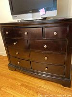 Front view of nine drawer dark wood dresser with a TV on top, showing scratches and wear on surface.