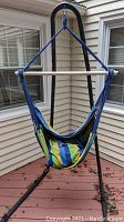 Full view of hammock with colorful striped cushion suspended on black metal tubular stand on a wooden deck.