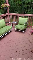 Patio furniture set shown on wood deck including two armchairs with green cushions and loveseat also with green cushions. Metal frames show oxidation.