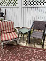 Photo of two patio chairs and a small square table between, showing one cushioned striped and one mesh chair