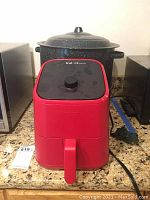 Red Instant Vortex Mini air fryer on kitchen counter next to appliances and large enamel pot in background.