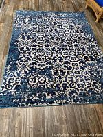 Full view of the rectangular blue and white patterned area rug on wood floor showing overall condition and design.
