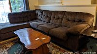 Overall view of the brown L-shaped sectional sofa in a living room setting with patterned rug and wooden coffee table.