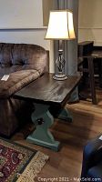 Solid wood side table with dark top and green painted base, positioned next to couch on hardwood floor.