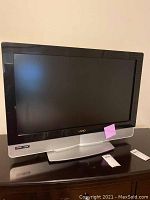 Front view of Vizio TV, showing screen, black bezel, silver base, and remote control on table.