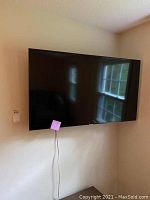 Front view of Samsung flat screen TV mounted on wall showing screen surface and part of room reflection.