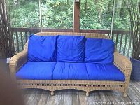Wicker sofa with natural wicker frame and blue cushions viewed from the front with outdoor screened porch background.