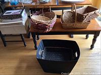 Wide shot of various woven baskets placed on wooden tables and a black fabric tote on the floor in front, showing the lot contents